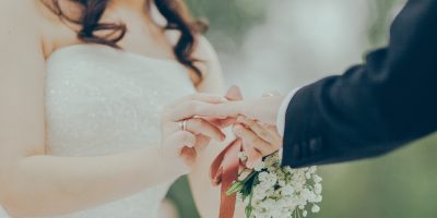 Frau trägt Brautkleid und hält die Hand ihres Ehemanns.