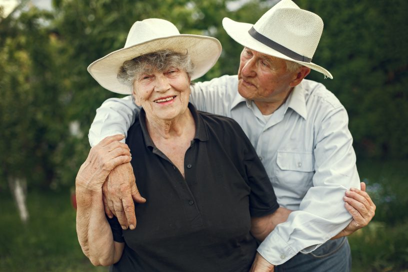 Älteres Ehepaar liegt sich lächelnd in den Armen.